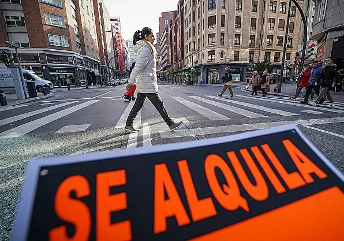 Cartel de alquiler delante de una calle con edificios de viviendas